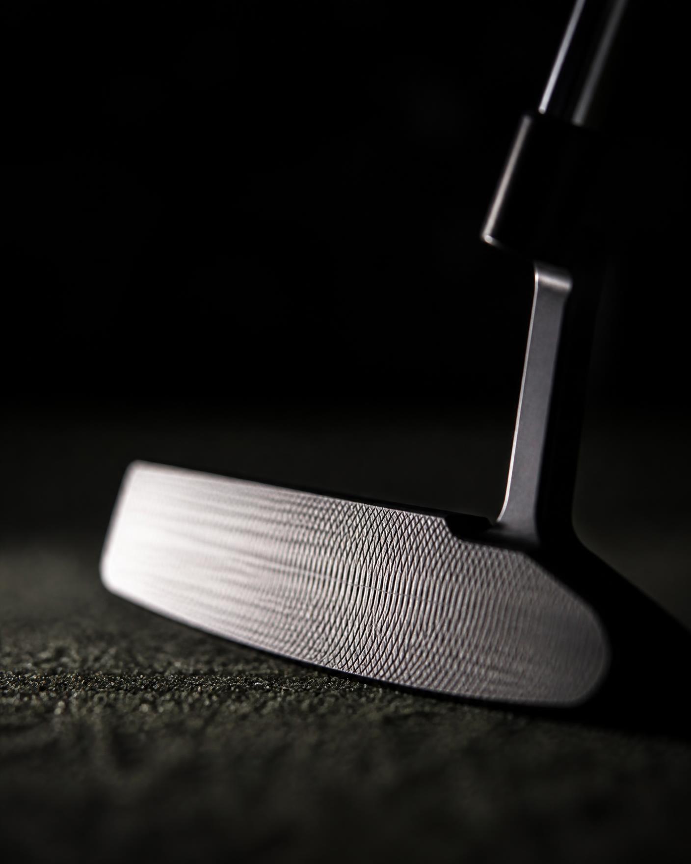 Blade putter head on a dark green with nothing attached to the club